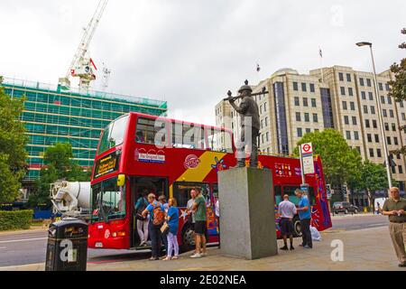 Der rote Tourbus hielt an der Haltestelle Tower Hill und die Bronzestatue des Building Worker neben der Bushaltestelle London, England, London, UK 2016 Stockfoto