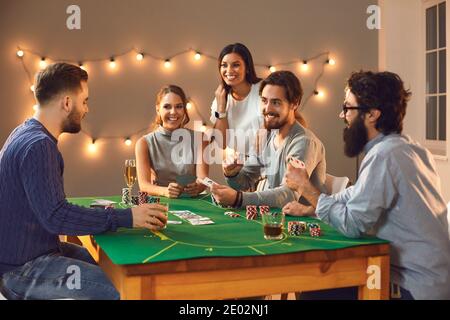 Fröhliche Gesellschaft von männlichen und weiblichen Freunden, die an einem Pokertisch sitzen und den Abend genießen. Stockfoto
