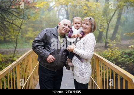 Glückliche Großeltern mit kleinen kleinen Enkelin im schönen Herbstpark Stockfoto