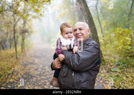 Happy Großvater hält niedlichen Enkelkind im Herbst Park Stockfoto