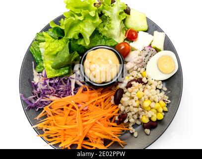 Gesunder Gemüsesalat mit frischen Tomaten, Karotten, grüner Eiche, Mais, Hirse, Ei, purpurem Kohl und Salatdressing auf schwarzem Teller. Diät-Menü. Vegan Stockfoto