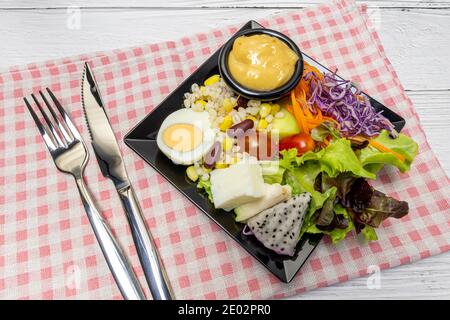 Gesunder Gemüsesalat mit frischen Tomaten, Karotten, grüner Eiche, Mais, Hirse, Ei, purpurem Kohl und Salatdressing auf schwarzem Teller. Diät-Menü. Vegan foo Stockfoto