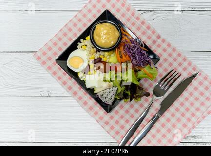 Gesunder Gemüsesalat mit frischen Tomaten, Karotten, grüner Eiche, Mais, Hirse, Ei, purpurem Kohl und Salatdressing auf schwarzem Teller. Diät-Menü. Vegan foo Stockfoto