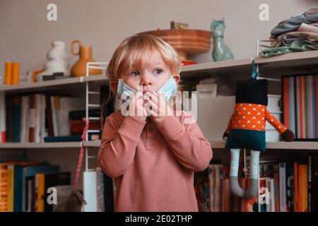 Zwei Jahre altes Kind versucht, auf Gesichtsmaske zu Hause setzen. Mittlere Aufnahme. Vorderansicht. Stockfoto