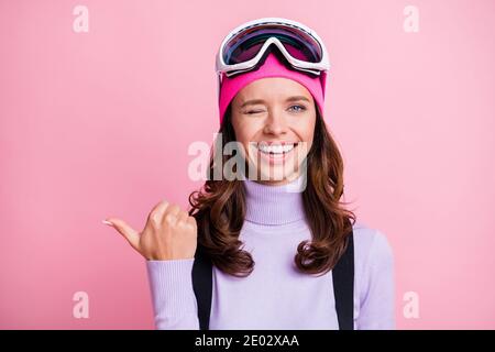 Foto-Porträt von winking Mädchen zeigt Daumen auf leeren Raum Isoliert auf pastellrosa Hintergrund Stockfoto