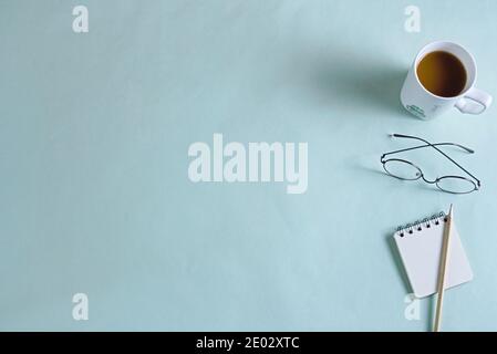Kaffeetasse, Gläser, Notizbuch, Bleistift liegen flach auf blauem Hintergrund, Textraum kopieren Stockfoto