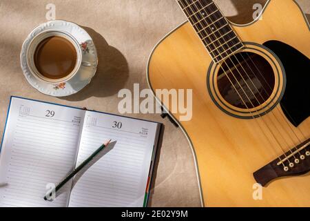 Coronavirus, Covid-19, Arbeitsplatz eines zu Hause isolierten Musikers, Gitarre, Kaffee und Bleistift auf leerem Notizbuch Stockfoto