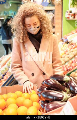 Sevilla, Spanien, 23. Dezember 2020: Eine Frau, die eine schützende Gesichtsmaske trägt, kauft Obst auf einem Markt. Stockfoto