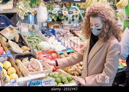 Sevilla, Spanien, 23. Dezember 2020: Eine Frau, die eine schützende Gesichtsmaske trägt, kauft Obst auf einem Markt. Stockfoto