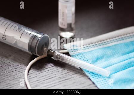 Spritze, Fläschchen und chirurgische Gesichtsmaske auf einem schwarzen Tisch. Hintergrund des Covid- oder Coronavirus-Impfstoffs Stockfoto