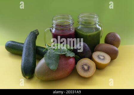 Smoothies mit frischen Kiwis, Spinat, Zucchini und Avocado.Konzept der gesunden grünen und roten Detox-Getränke in Einmachglas auf grünen und gelben kreativen Rücken Stockfoto