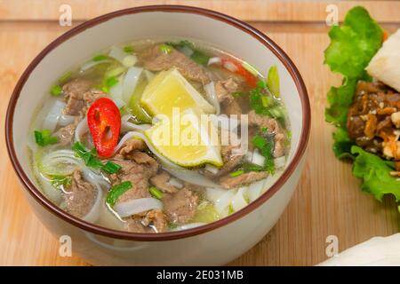 Würzige Pho-Suppenschüssel mit Rindfleisch, Zitronenscheibe und Chilischoten auf Holztisch. Lieferung nach Hause Stockfoto