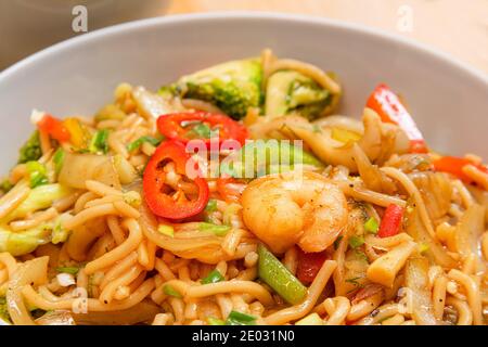 Goldfarbene würzige Meeresfrüchte-Nudeln mit Garnelen, Brokkoli, Chili in einem Teller auf einem Holztisch Stockfoto
