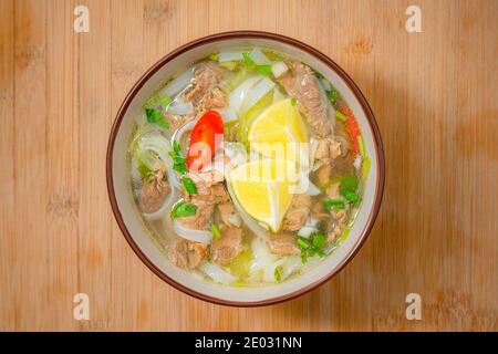 Würzige Pho-Suppenschüssel mit Rindfleisch, Zitronenscheibe und Chilischoten auf Holztisch. Lieferung nach Hause Stockfoto