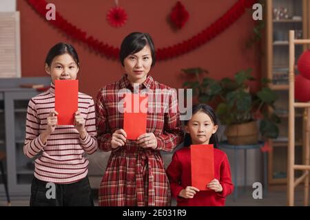 Familienportrait der schönen reifen chinesischen Frau und ihre Töchter stehen im Wohnzimmer mit roten Umschlägen, Lunar New Year Konzept Stockfoto