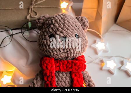 Braun gestrickter Teddybär mit rotem Schal liegt darauf Die Tabelle Stockfoto