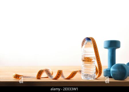Sport und gesundes Leben Konzept mit Kurzhantel Wasserflasche und Maßband auf Holzparkett mit großem Fenster im Hintergrund. Vorderansicht. Horizont Stockfoto