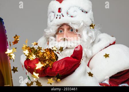 Weihnachtsmann mit goldenen Sternen Konfetti auf seinen Handflächen in Fäustlingen feiern Weihnachten und Neujahr, close up Studio Portrait Stockfoto