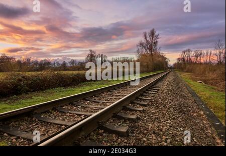 Diagonal Bahngleise in ländlichen Szene führt in fernen bunten Sonnenuntergang. Stockfoto