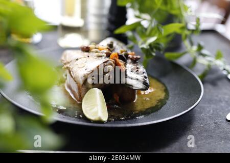 Geröstete Makrele. Ganzer Fisch mit Knoblauch, Oliven und Zitrone serviert. Appetitliches Gericht auf einem schwarzen Teller serviert.kulinarische Fotografie, Lebensmittel-Fotografie. Stockfoto