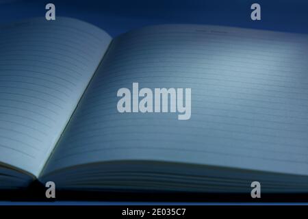 Nahaufnahme eines leeren geöffneten Buches auf dunklem Holzhintergrund mit weichen Schatten am Abend oder in der Nacht. Klassisches blaues Bild Stockfoto