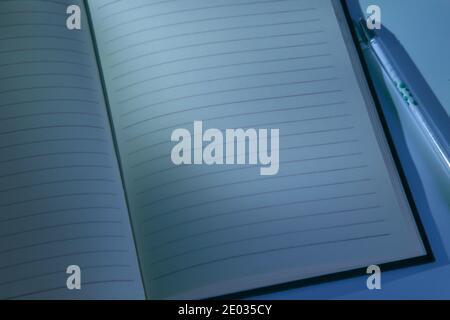 Nahaufnahme von Stift und geöffnetem Buch mit weichen Schatten am Abend oder in der Nacht. Klassisches blaues Bild, leer für Text Stockfoto