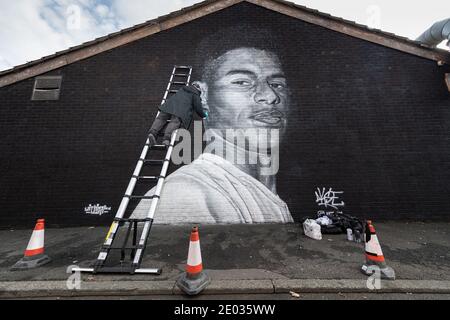 Street Artist Akse, steht vor seinem Wandbild des Fußballstars Marcus Rashford. Stockfoto