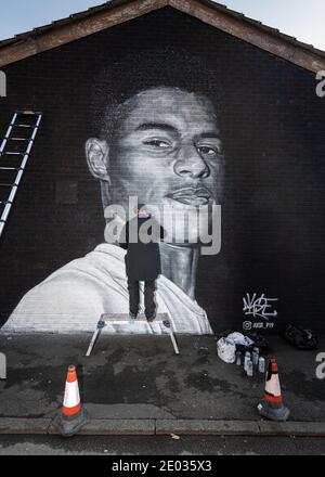 Street Artist Akse, steht vor seinem Wandbild des Fußballstars Marcus Rashford. Stockfoto