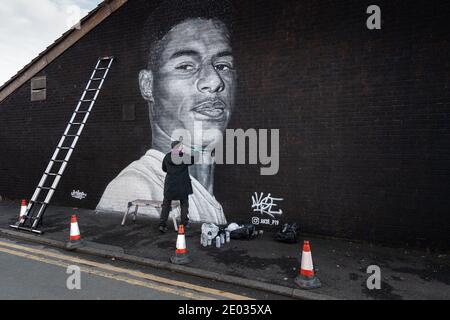 Street Artist Akse, steht vor seinem Wandbild des Fußballstars Marcus Rashford. Stockfoto