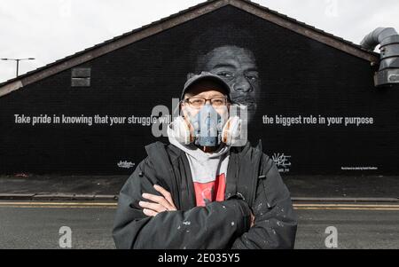 Street Artist Akse, steht vor seinem Wandbild des Fußballstars Marcus Rashford. Stockfoto