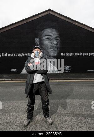 Street Artist Akse, steht vor seinem Wandbild des Fußballstars Marcus Rashford. Stockfoto