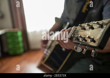 Nahaufnahme der Hände des Menschen spielen Gitarre drinnen, Hobby und Lernen, Fokus auf Vordergrund Stockfoto