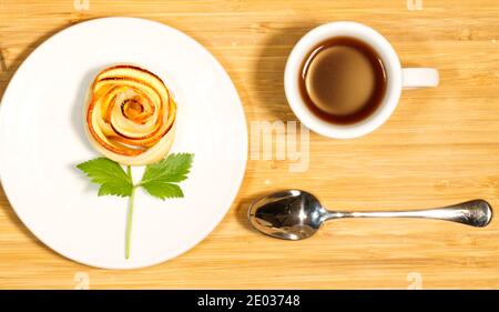 Kaffeetasse, hausgemachtes schmackhaftes roséförmiges Apfelgebäck auf Holztisch, Nährstofffrühstück, Draufsicht Stockfoto