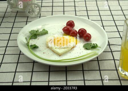 Nährstoff gesundes Frühstück. Herzförmiges Spiegelei, Kirschtomaten in Teller auf karierter Tischdecke Stockfoto