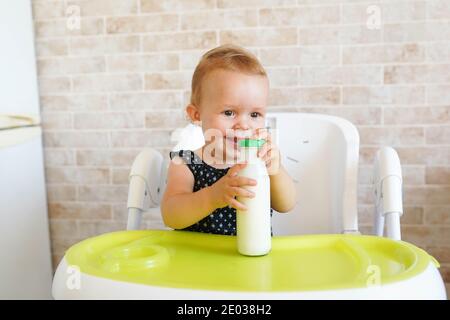 Smilling Baby hält eine Flasche Milch in der sonnigen modernen Küche, Ernährung Abendessen für Kinder Stockfoto