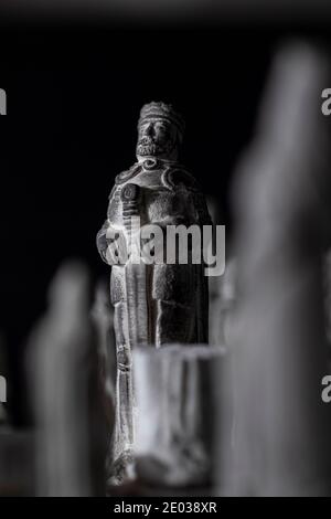 Ein schwarz-weißes Porträt einer Steinskulptur eines Königs auf einem Schachbrett zwischen anderen Schachfiguren. Es ist das wichtigste Stück in dieser Strat Stockfoto