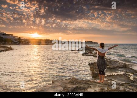 Meditierende Frau auf felsigen Ufer während des Sonnenuntergangs Stockfoto