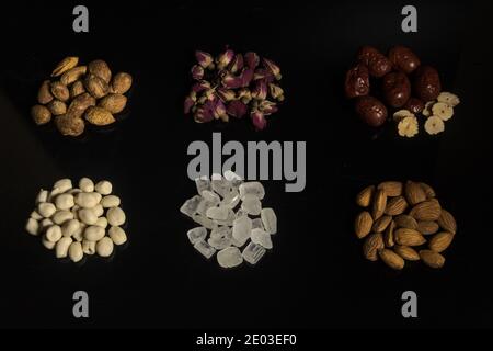 Sechs Zutaten auf schwarzem Hintergrund, Rosen, rote Datteln, Rock Bonbons, Erdnüsse, Mandeln Stockfoto