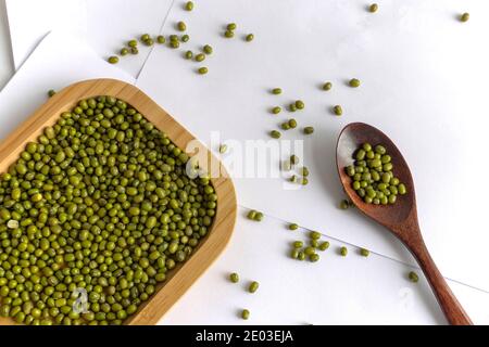 Mungbohnen auf weißem Hintergrund, grünes Gramm auf Holzkiste und Löffel Stockfoto