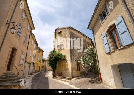 Eine Y-Kreuzung in Lourmarin mit seltsam geformten Steingebäuden Und blauer Verschluss mit blauem Himmel oben und Kopfsteinpflaster Straßen darunter Stockfoto