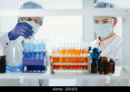 Wissenschaftler in Schutzmasken stehen vor einem Rack von Reagenzgläsern . Stockfoto