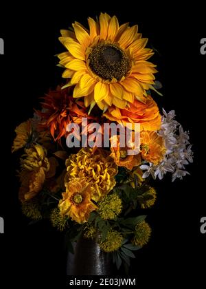 Blumenstrauß aus herbstlichen gelben, orangen und weißen Blüten in einer silbernen Vase isoliert auf schwarzem Hintergrund. Stockfoto