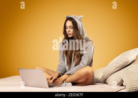 Attraktive junge Frau trägt Kigurumi Schlafanzug, arbeitet auf ihrem Laptop Stockfoto