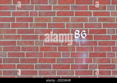 Hausnummer 86 in weiß auf einer roten Backsteinmauer geschrieben. Stockfoto