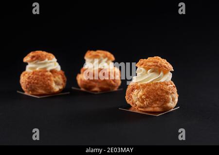 Drei leckere frische knusprige Profiterolen mit süßer weißer Creme im Inneren. Nahaufnahme von hausgemachten leckeren Eclare isoliert auf schwarzem Hintergrund. Konzept der Desserts, Restaurant Essen. Stockfoto