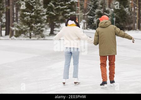 Rückansicht eines Paares in warmer Kleidung, das zusammen auf dem Schlittschuh ist Eisbahn im Winter Stockfoto