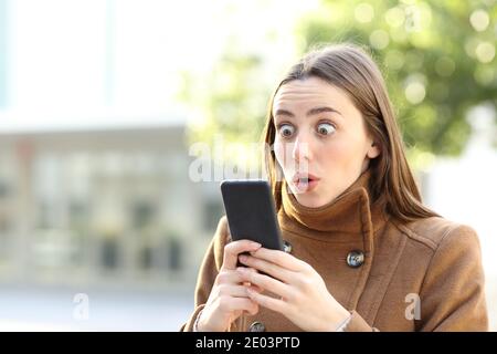 Staunende Frau, die im Winter auf dem Handy steht Straße Stockfoto