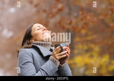 Glückliche Frau mittleren Alters atmend hält Kaffeebecher beim Frühstück In einem Park im Herbst Stockfoto