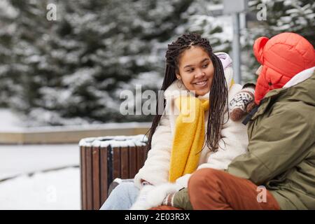 Junge glückliche Frau im Gespräch mit ihrem Freund, während sie sitzen Auf der Bank im Park Stockfoto