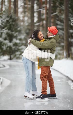 Glückliches junges Paar umarmt sich gegenseitig stehen auf Eisbahn Im Winter im Freien Stockfoto